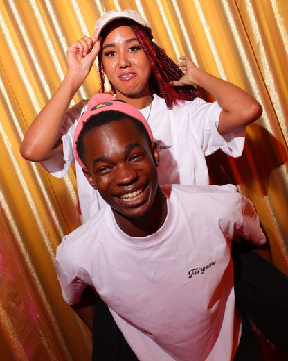 Two people wearing white t-shirts with pink caps against a yellow curtain background