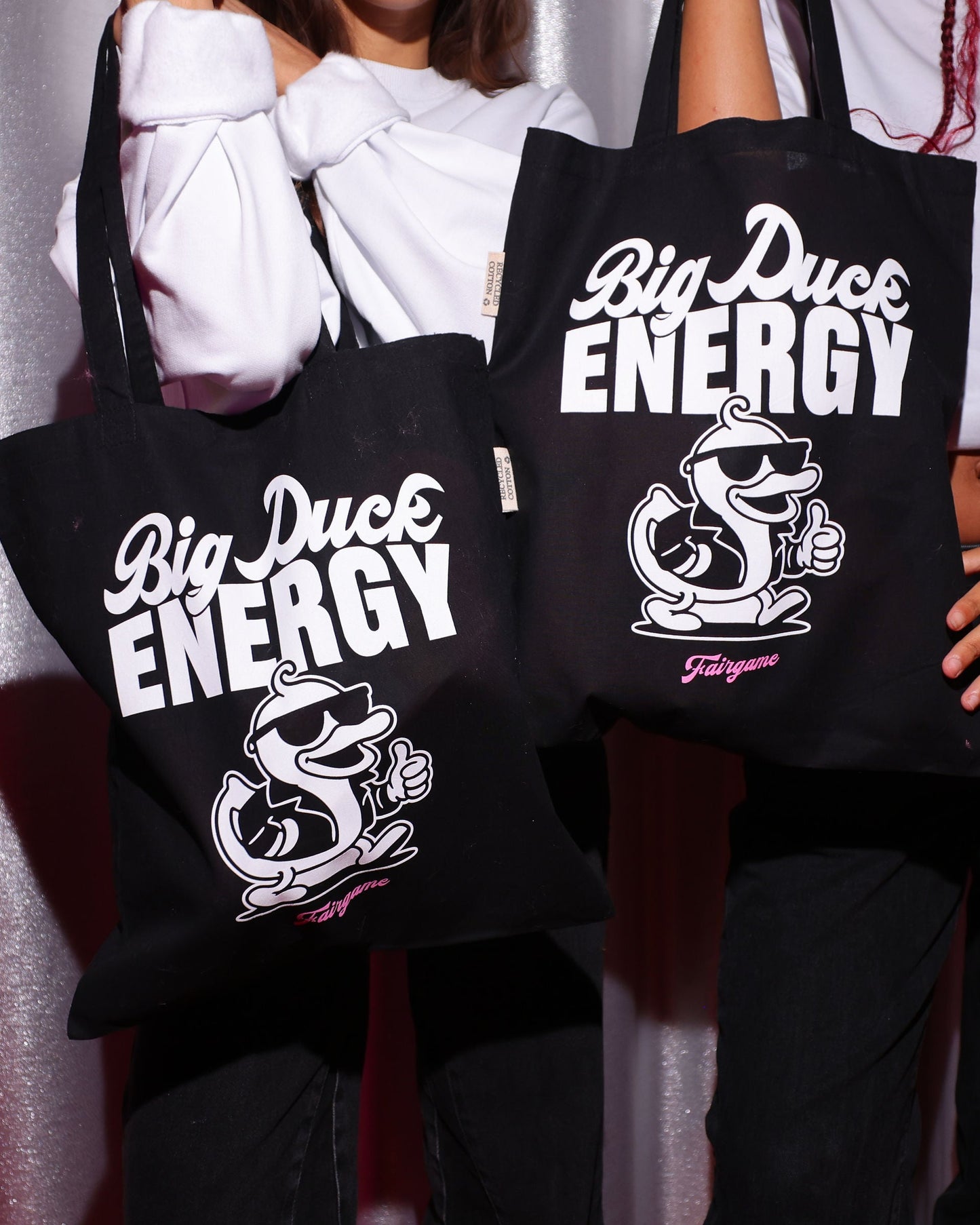 Two people holding black tote bags with 'Big Duck Energy' branding against a plain background
