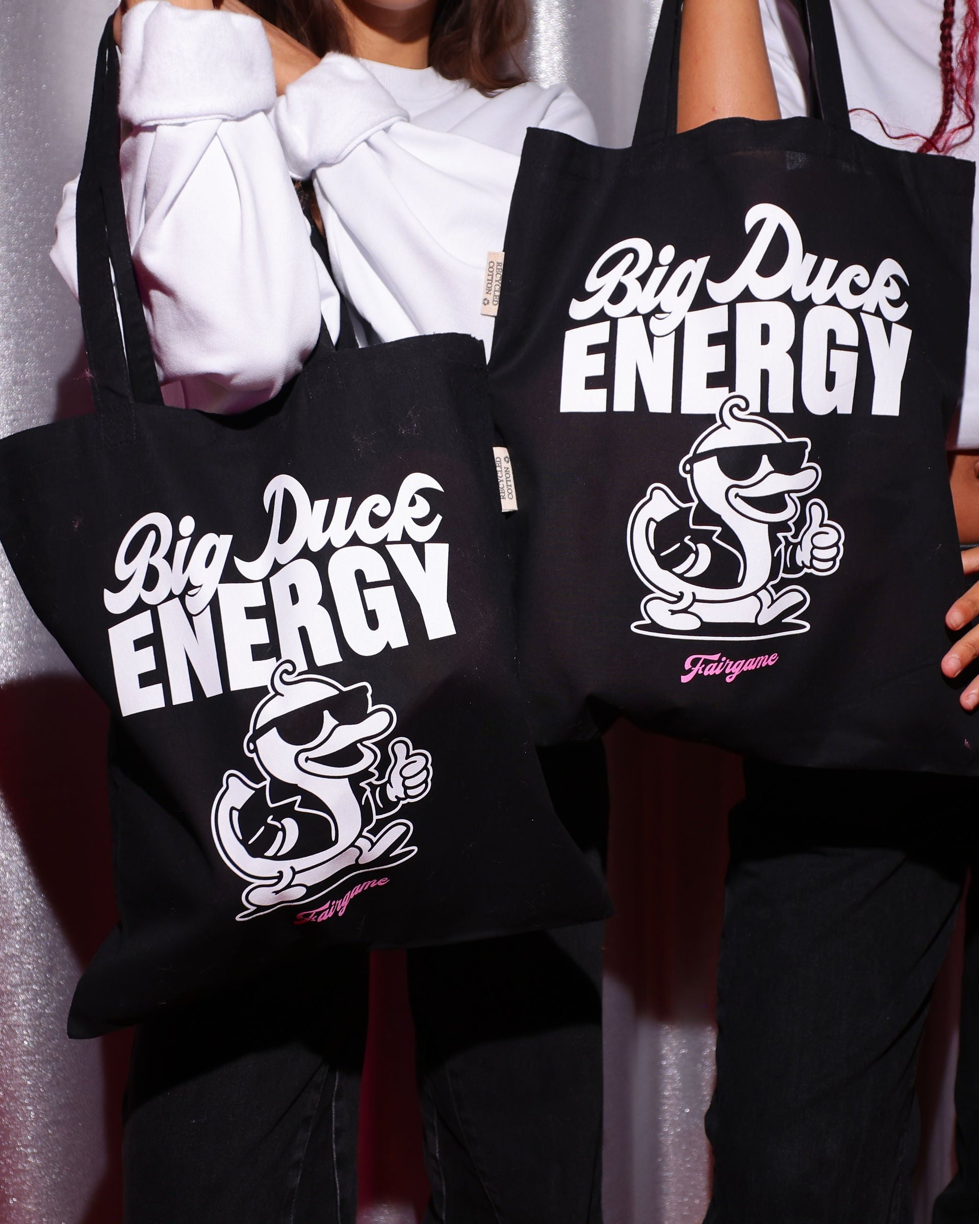 Two people holding black tote bags with 'Big Duck Energy' branding against a plain background