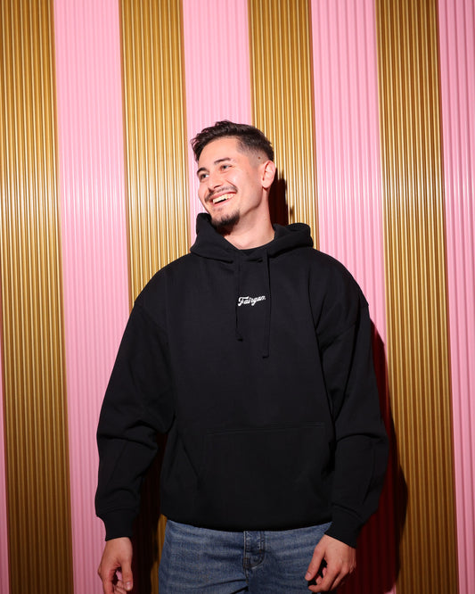 Person wearing a black hoodie with a logo against a striped pink and gold background